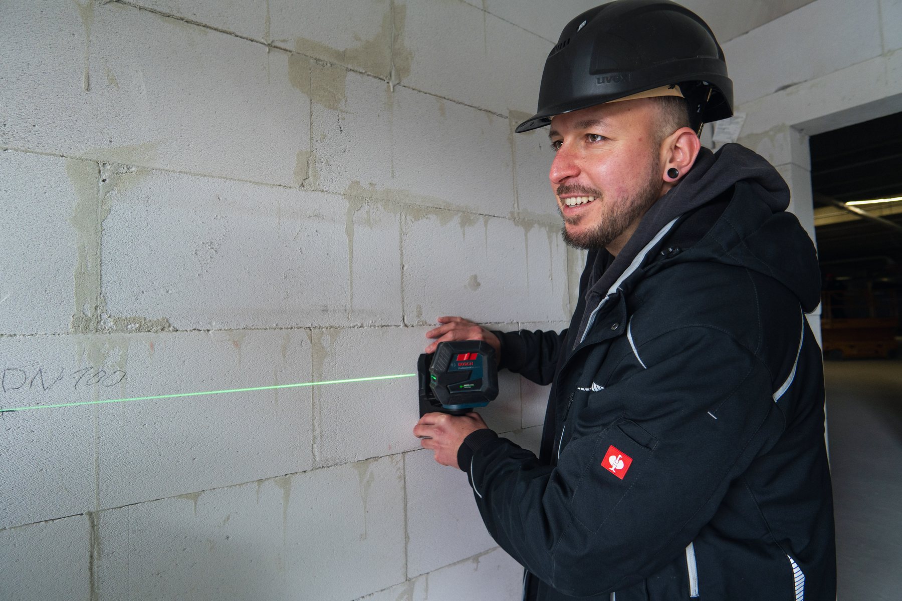 Zwei Monteure nehmen mit einem Laser Maß an einer Wand.